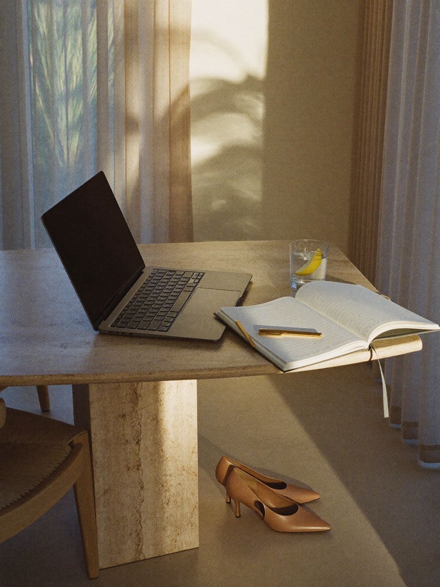A closed laptop on a travertine table and a pair of heels left beside it