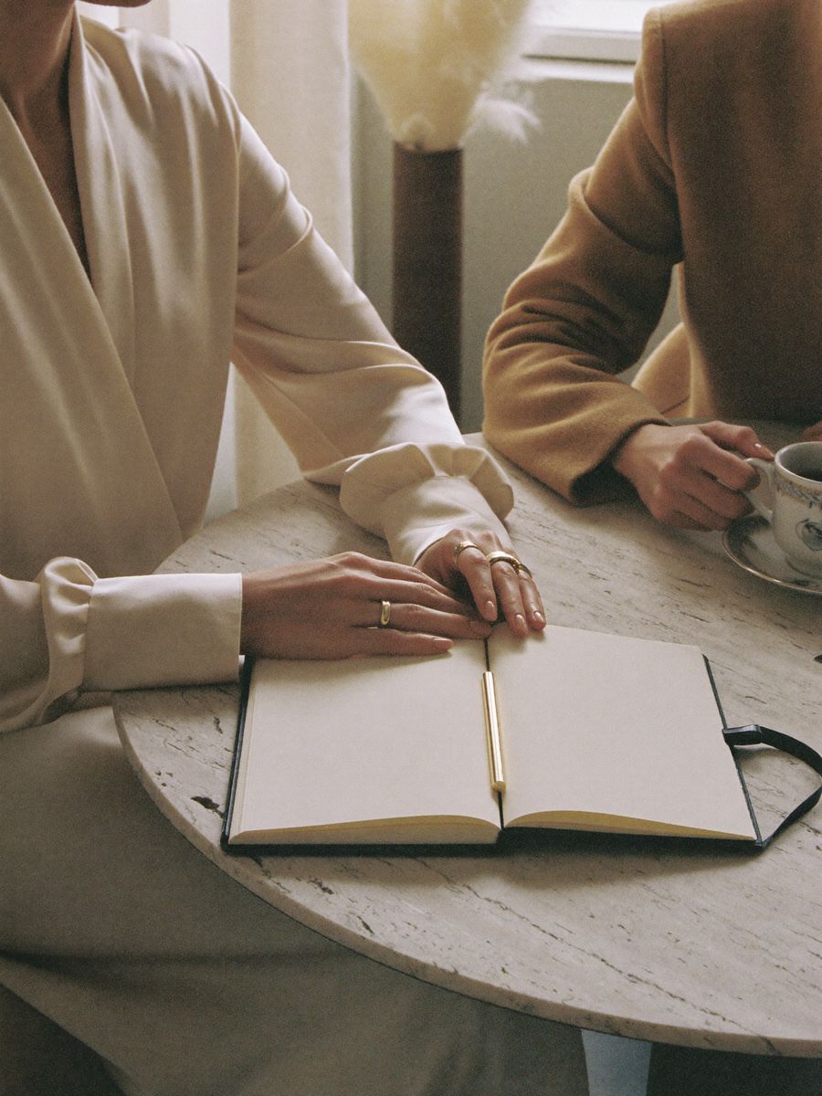 Two women at a round travertine table with an open notebook and tea